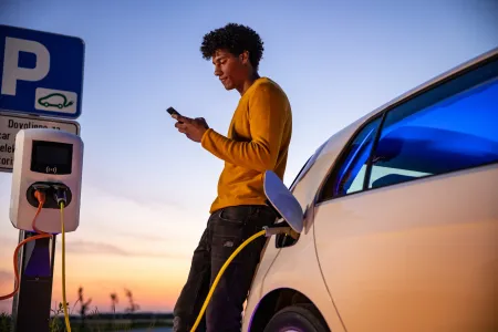 Man on cell phone standing by car at EV charging station