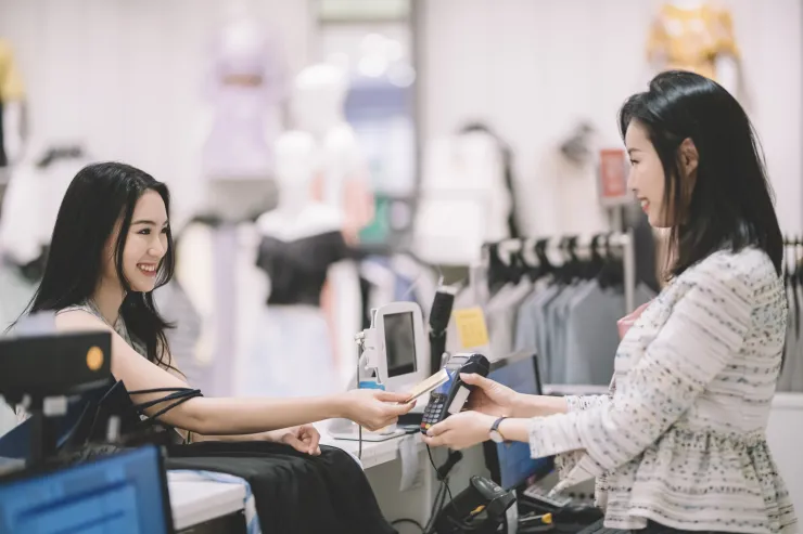 An asian chinese young woman buying clothes from a clothing store at the cashier hand over her credit card for payment through credit card reader from the sales clerk